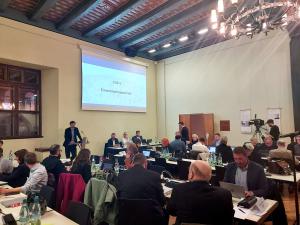 Stadtratsmitglieder sitzen an Tischen im Historischen Rathaus, ein Redner steht am Rednerpult