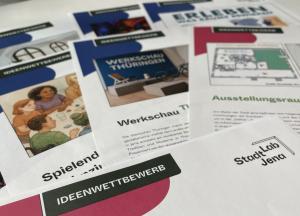 Auf einem Tisch liegen mehrere Broschüren zum Ideenwettbewerb 2025