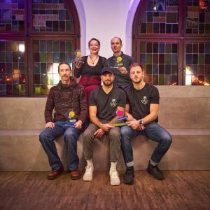 Die Gewinnerinnen und Gewinner des StadtLab Ideenwettbewerbs 2025: Fünf PErsonen sitzten mit dem Preis auf Stufen.