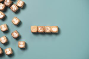 Mehrere Holzwürfel auf einem blauen Hintergrund, die Symbole für E-Mail, Telefon und Personen enthalten