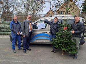 drei Männer und eine Frau stehen mit einem Spendenscheck und einem Weihnachtsbaum vor einem Auto.