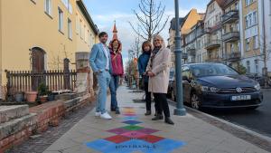 Ein Mann und drei Frauen stehen an einem bunten Hüpfekästchen.