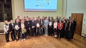 Gruppe von Menschen steht auf der Bühne und lacht in die Kamera.