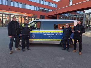 Vier Männer stehen vor einem Auto der Ordnungsbehörde und sehen in die Kamera.