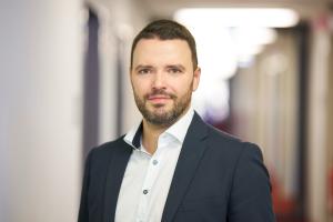 Mann steht in einem Korridor und lächelt in die Kamera