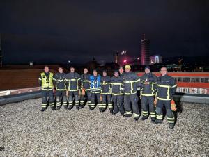 Mehrere Feuerwehrmänner schauen in die Kamera, im Hintergrund Feuerwerk.