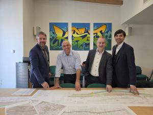 Vier Männer sind zeigen auf Baupläne und schauen in die Kamera.