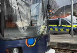 Blick auf eine Straßenbahn mit gesprungener Frontscheibe. Im Hintergund steht ein Polizeiauto.