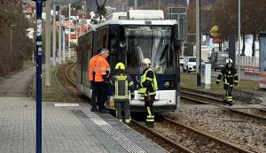Eine Straßenbahn steht auf den Gleisen mit gesprungener Frontscheibe. Drei Feierwehrleute und zwei Männer in orangfarbener Weste begutachten den Schaden.