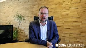 Ein Mann sitzt an einem Tisch und spricht direkt in eine Kamera.