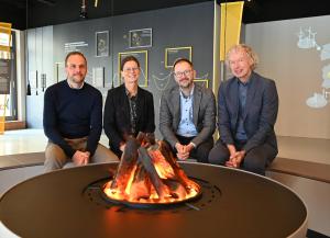 Drei Männer und eine Frau sitzen an einem künstlichen Lagerfeuer in einer Ausstellung.