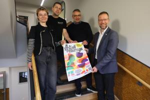 Vier Menschen halten ein Plakat und lachen in die Kamera.