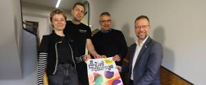 Vier Menschen halten im Treppenhaus ein Plakat.