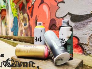 Vier Spraydosen vor einer besprühten Wand