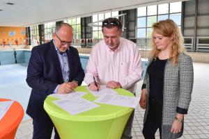 In der ehemaligen Schwimmhalle unterzeichnen  (v. l.) Bernhard Dengel (Geschäftsführer Jenaer Bäder), Jörg Hühn (Geschäftsführer reCoVer Stiftung Jena) und Katrin Hitziggrad (Blank – Agentur für Zwischennutzung) den Kooperationsvertrags an einem Stehtisch.