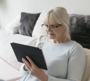 Seniorin sitzt auf einer Couch und surft mit einem Tablet