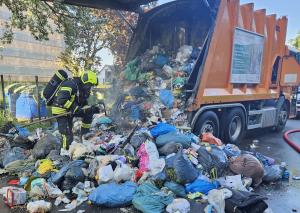 Ein Müllfahrzeug hat den Abfall auf eine Straße gekippt, nachdem die Ladung gebrannt hat. Ein Feuerwehrmann durchsucht den Müll nach Glutnestern.