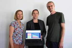 Zwei Frauen und ein Mann stehen nebeneinander. Eine Frau hält einen offenen Laptop, der das digitale Klimamonitoring der Stadt Jena zeigt.