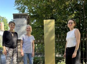 Drei Personen stehen neben einer Stele