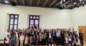 eine Gruppe von Menschen steht vor einer Wand mit zwei Fenstern und feiert ihre Einbürgerung im historischen Rathaus