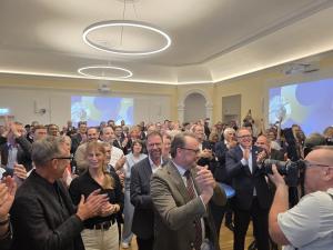 Menschen stehen in einem Saal und klatschen in die Hände.