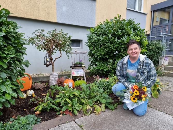 Preisträgerin Kathy Witte hockt neben einem Blumenbeet, welches zu der Grünen Oase gehört, die sie geschaffen hat.