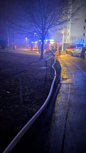 Blick auf eine Straße mit Plattenbauten. Davor stehen Feuerwehrautos mit Blaulicht