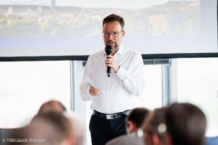 Ein Mann steht vor einem Publikum und spricht in ein Mikrofon.