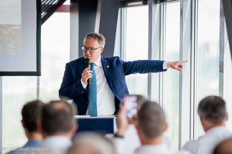 Ein Mann spricht in ein Mikrofon vor einem Publikum.