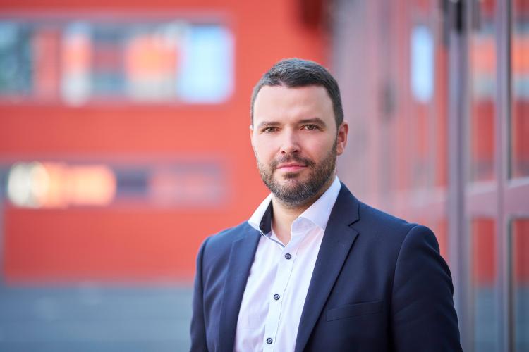 Mann in blauem Anzug steht im Außenbereich und lächelt