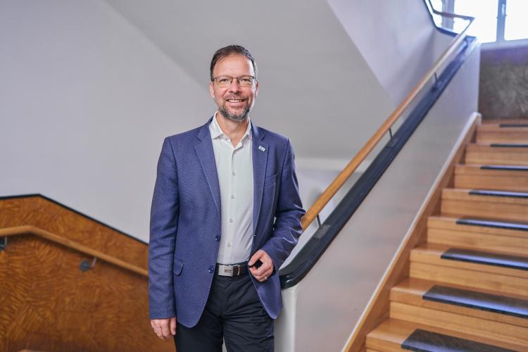 Mann in blauem Anzug steht in einem Treppenhaus und lächelt