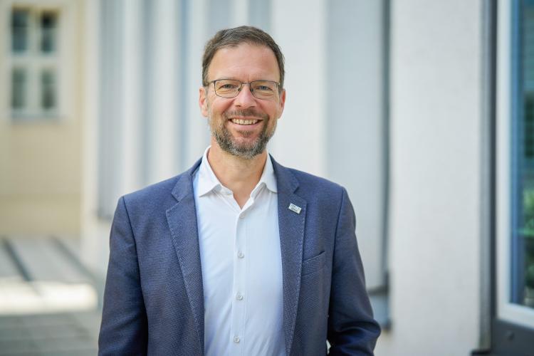 Mann in blauem Anzug steht im Außenbereich und lächelt