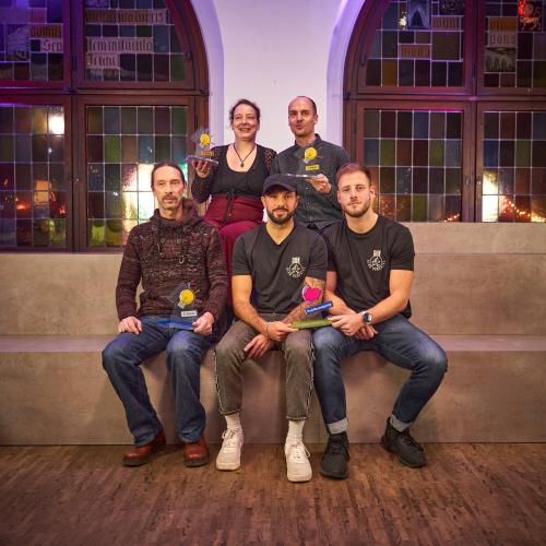 Die Gewinnerinnen und Gewinner des StadtLab Ideenwettbewerbs 2025: Fünf PErsonen sitzten mit dem Preis auf Stufen.