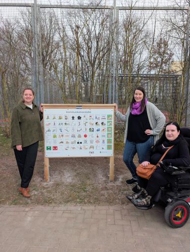 Kathleen Lützkendorf (Dezernentin für Soziales, Gesundheit, Zuwanderung und Klima),  Daniela Egert (Einreicherin des Vorschlags) und Ines Muskalla (Beauftragte für Menschen mit Behinderung der Stadt Jena) bei der Spielplatztafel im Marienwäldchen.