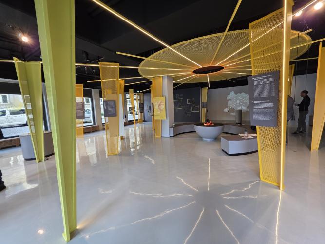 Blick in den Ausstellungsraum mit gelben Stelen und einem künstlichen Lagerfeuer.