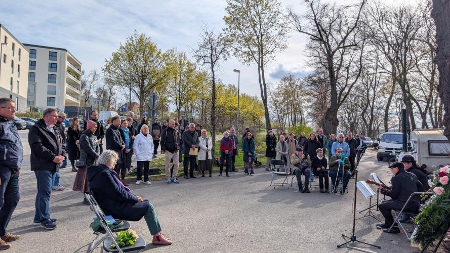 Mehrere dutzend Personen stehen und sitzen im Halbkreis um eine Musikgruppe.
