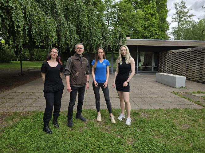 Ein Mann und drei Frauen stehen mit etwas Abstand vor dem Glashaus im Paradies.