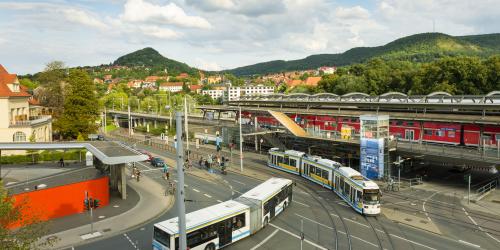 Eine Straße mit einem Bus und einer Straßenbahn, im Hintergrund ein Zug