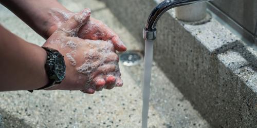 Zwei Hände die sich unter einem Wasserhahn mit laufenden Wasser waschen