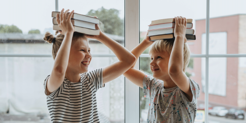 Zwei Kinder haben Bücher auf den Kopf und machen Faxen 