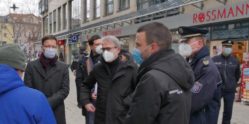 Fünf Menschen stehen in einer Straße mit vielen Läden, um Sie einige Polizisten und Journalisten