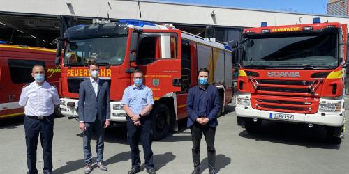 Feuerwehr im Hintergrund, im Vordergrund vier Männer mit Masken