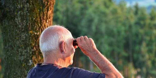 Ein Senior schaut durch ein Fernglas in die Weite