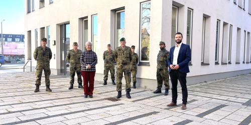 Mehrere Personen stehen im Außenbereich vor einem Gebäude. Einige tragen zivile Kleidung, einige tragen Bundeswehr-Uniform.