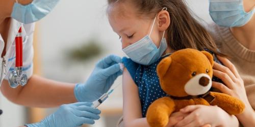 Ein Kind mit Teddy lässt sich impfen