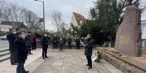 Menschen stehen vor einem Gedenkstein, ein Redner im Vordergrund