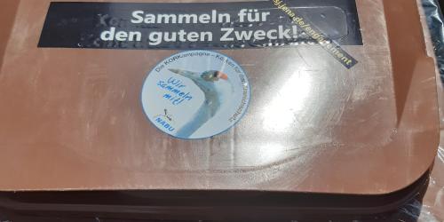 Auf dem deckel einer braunen Mülltonne kleben zwei Aufkleber, die auf die Korksammelaktion hinweisen.