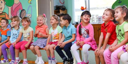 Lachende Kleinkinder sitzen im Kindergarten in einer Reihe