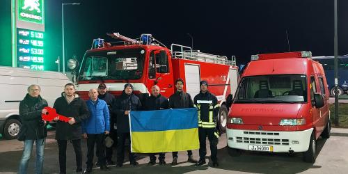 Menschen stehen vor mehreren Feuerwehrfahrzeuge