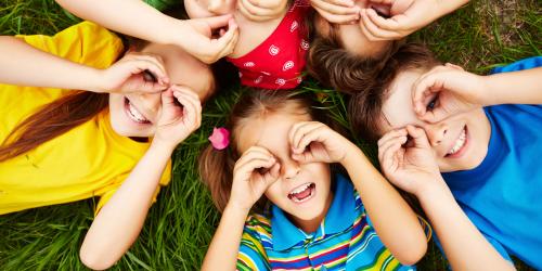 Fünf Kinder liegen im Kreis auf einer Wiese.